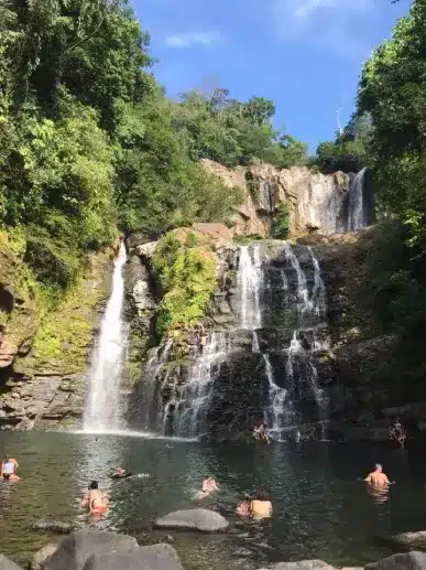 People Swimming at a Scenic Waterfall in the Jungle