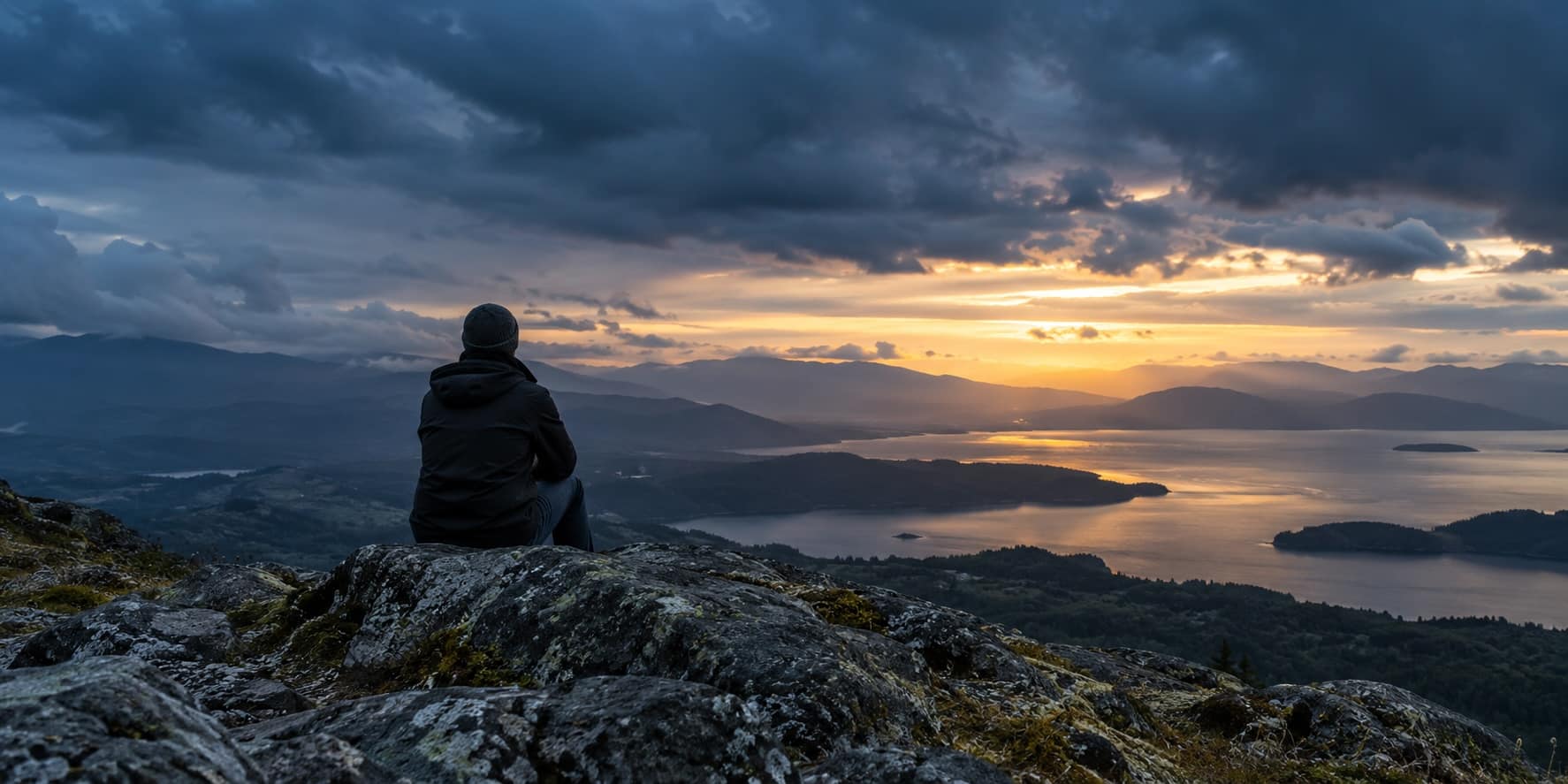 Person overlooking a lake beneath storm clouds as sunlight breaks across the horizon